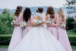 vista-posteriore-della-sposa-in-abito-da-sposa-e-damigelle-vestite-allo-stesso-modo-abiti-rosa-all-aperto